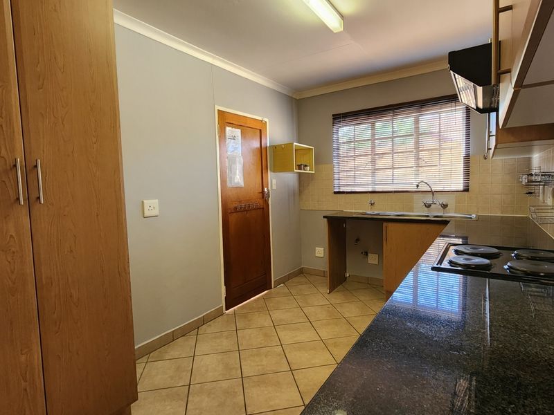 A functional kitchen featuring granite countertops, built-in cabinetry, an electric hob with extractor fan, and tiled flooring.