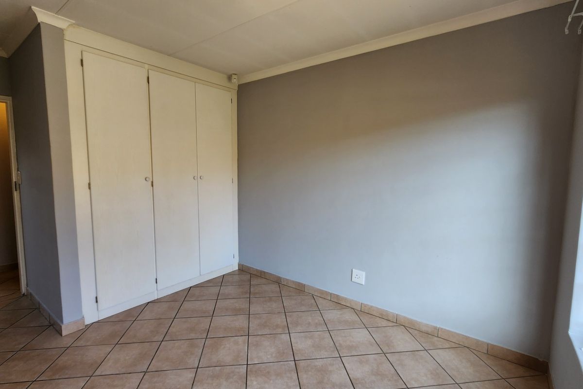 A vacant bedroom featuring neutral grey walls, tiled flooring, and built-in cupboards with security bars on the window.