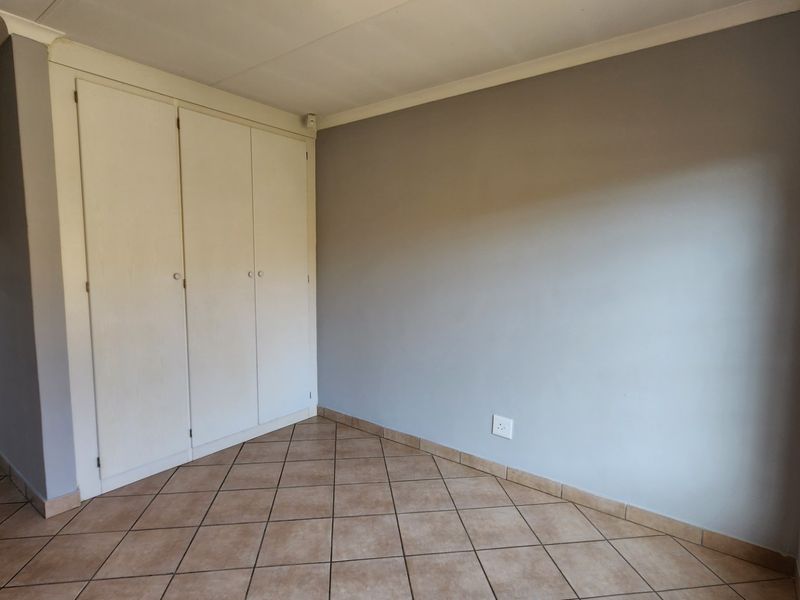 A vacant bedroom featuring neutral grey walls, tiled flooring, and built-in cupboards with security bars on the window.