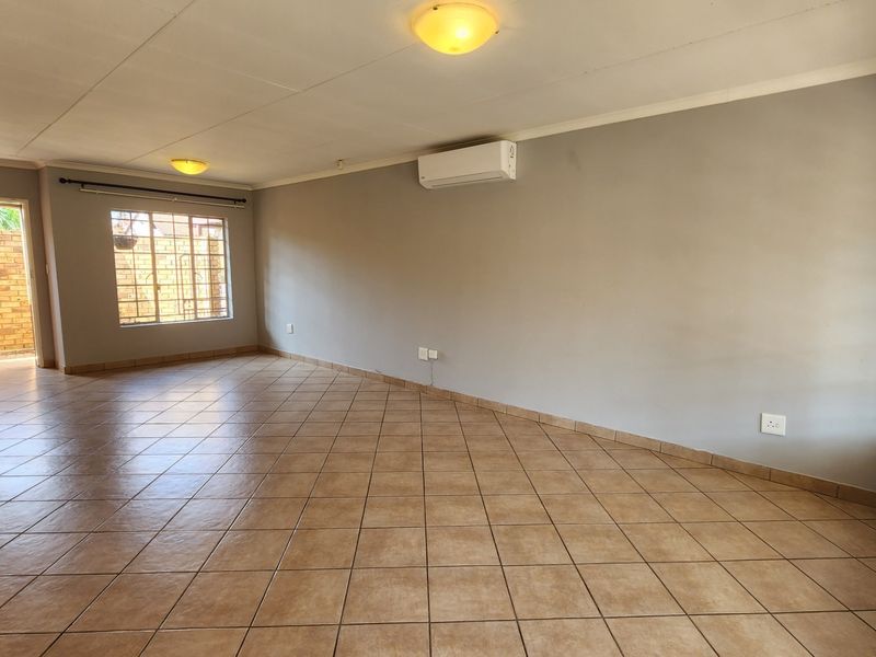 A spacious, empty living area featuring neutral grey walls, tiled flooring, and a wall-mounted air conditioning unit.