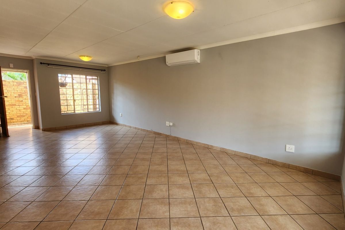 A spacious, empty living area featuring neutral grey walls, tiled flooring, and a wall-mounted air conditioning unit.