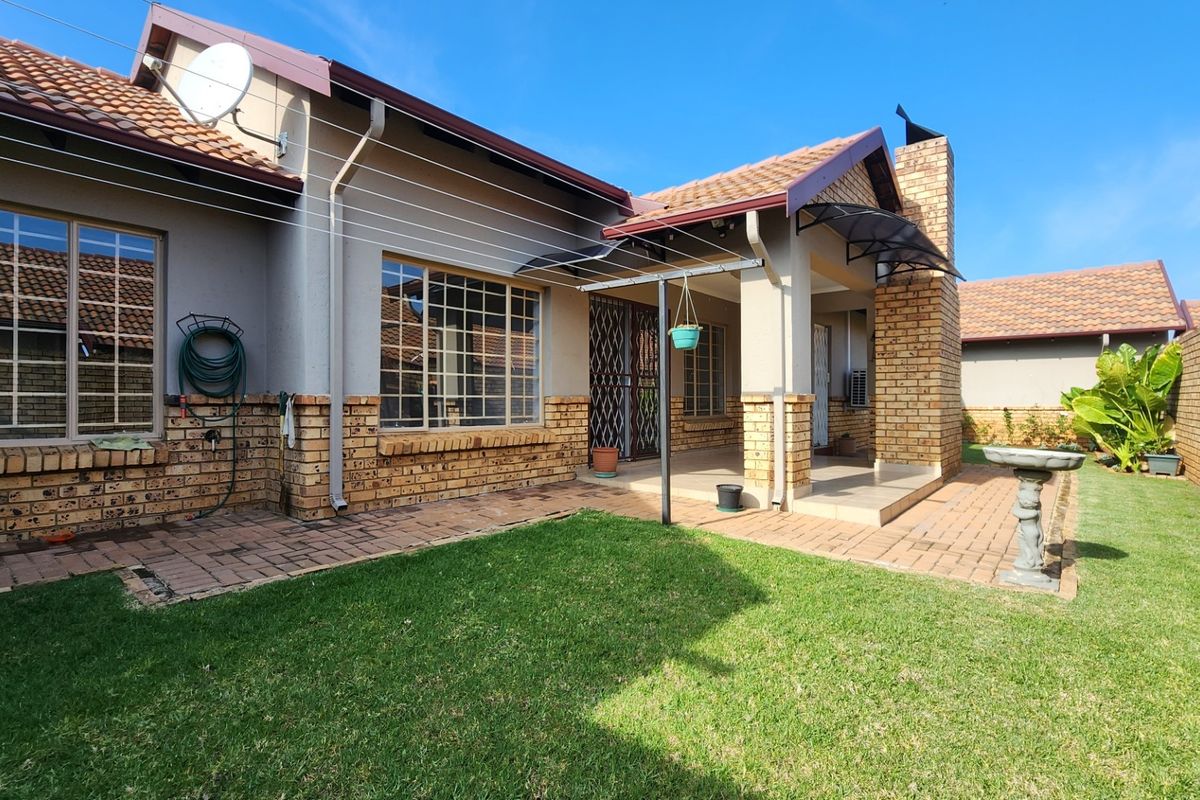 Rear view of the townhouse featuring a covered patio, brick facade, tiled roof, and a well-maintained private garden area.