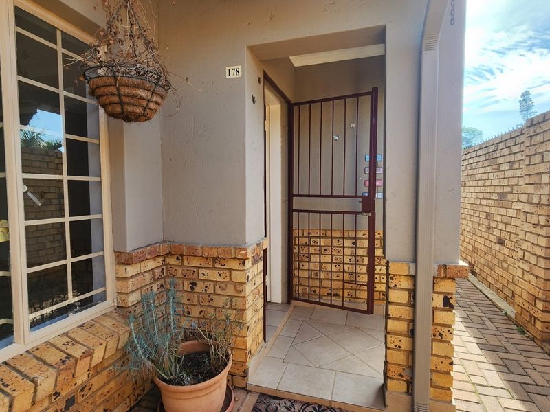 Front entrance area of the townhouse featuring a security gate, tiled porch, and brick facade detailing.