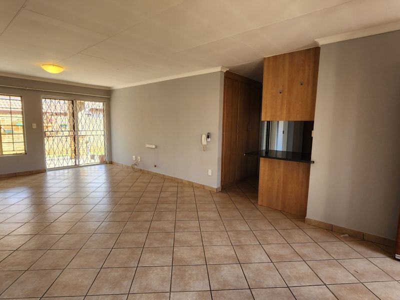 Spacious, open-plan living area featuring neutral tiled flooring, built-in storage cabinetry, and direct access to the exterior through a secure sliding door.