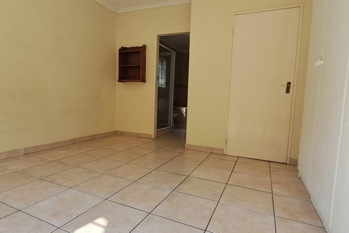 An empty bedroom featuring tiled flooring, a built-in wardrobe, and direct access to an adjoining bathroom.