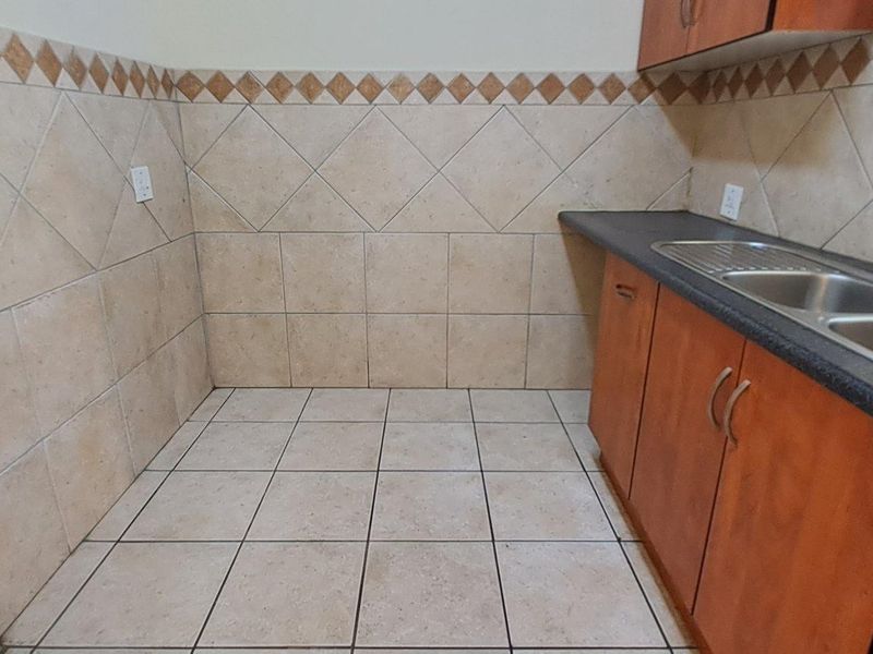 A functional laundry area featuring tiled walls and flooring, built-in wooden cabinetry, a double sink, and dedicated plumbing connections for appliances.