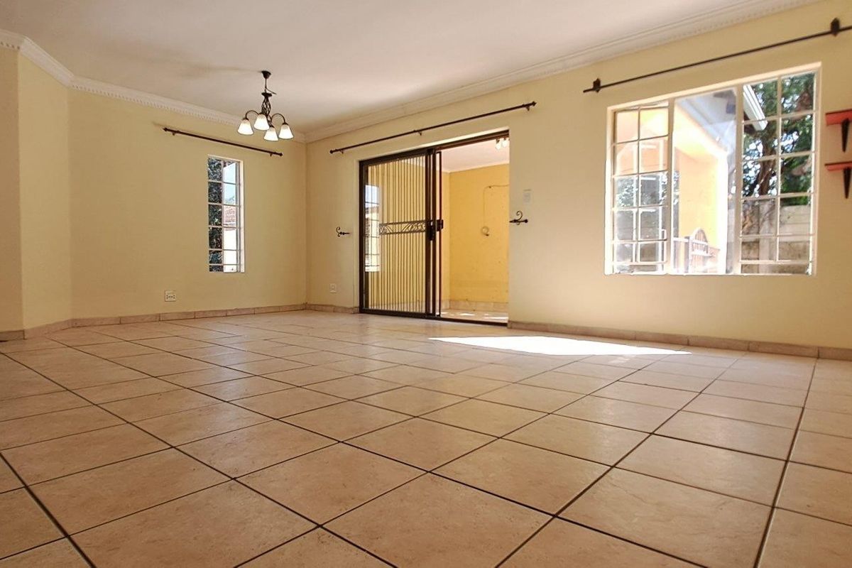 Spacious, empty living area featuring neutral ceramic floor tiles, natural light from multiple windows, and direct access to an outdoor patio through sliding doors.