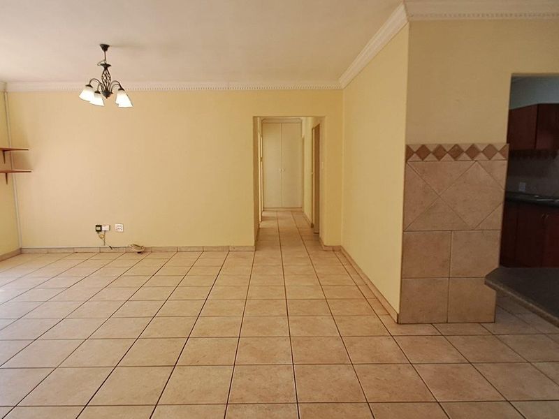 An open-plan living area featuring ceramic floor tiles, crown molding, and a view into the adjacent kitchen space.