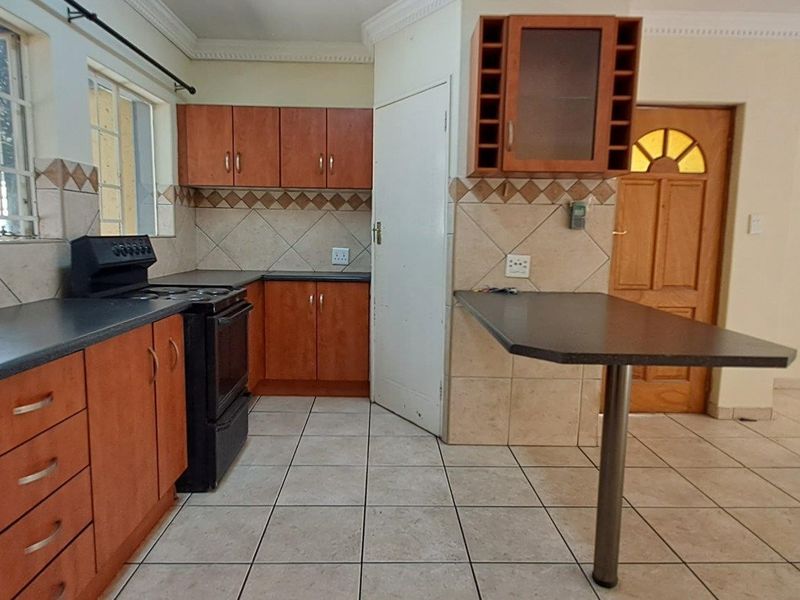 A functional kitchen featuring laminate cabinetry, tiled backsplash, a breakfast bar, and ceramic floor tiles, offering a clean and practical layout.