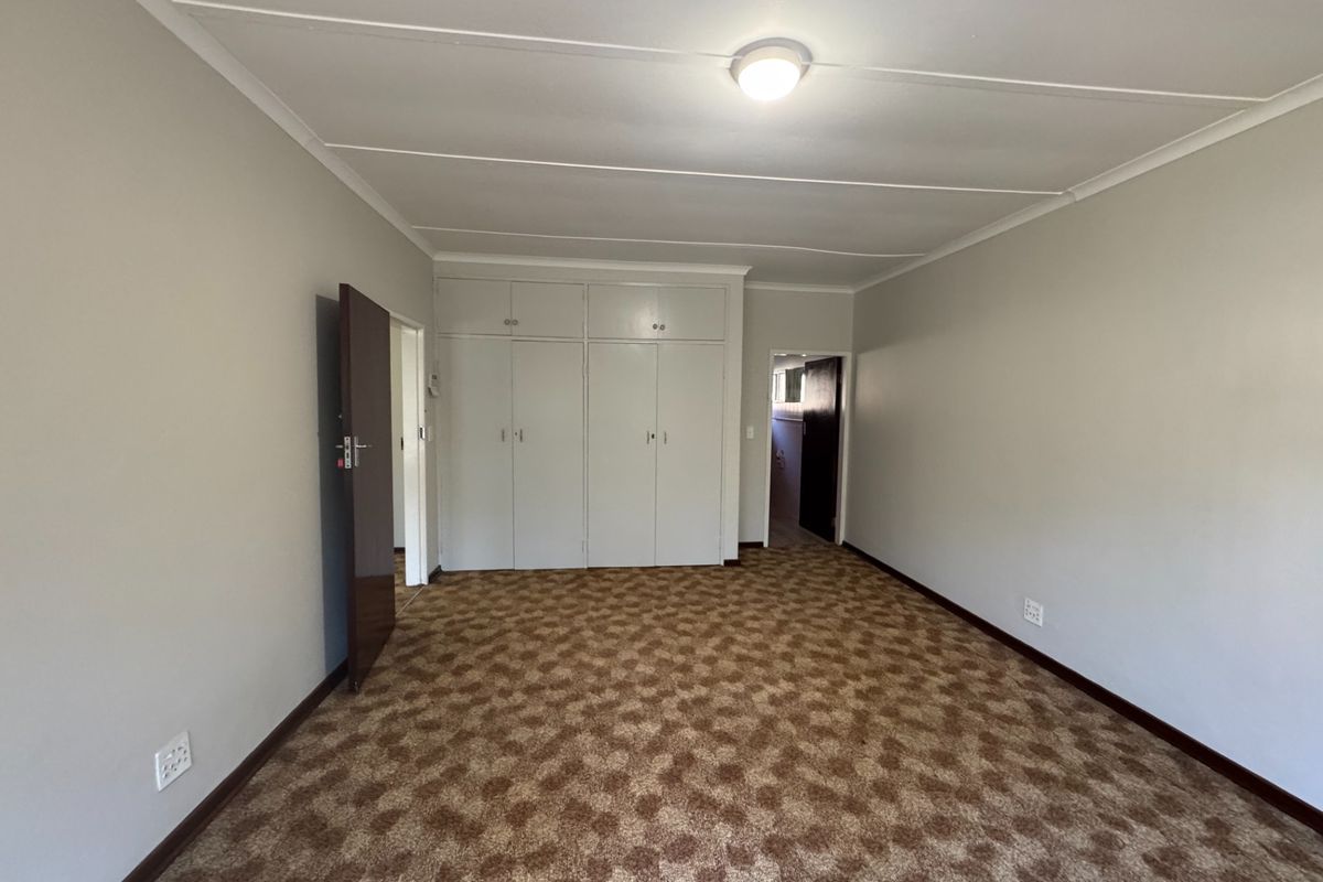 A spacious, empty bedroom featuring neutral walls, patterned carpet flooring, and ample built-in cupboard storage.