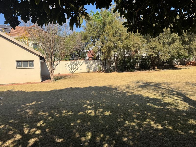 A spacious, well-established rear garden featuring a large lawn area, mature trees, and a secure boundary wall.