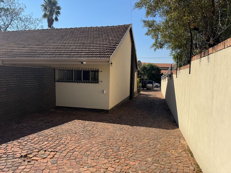 A view of the property's side entrance featuring a cobblestone driveway, tiled roof, and secure perimeter walling.