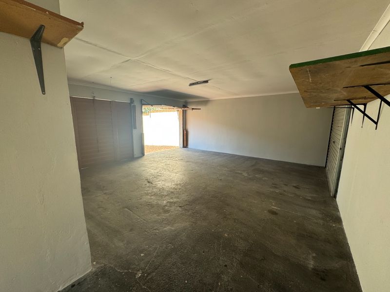 A spacious, empty double garage featuring concrete flooring, wall-mounted shelving brackets, and direct access to the exterior.