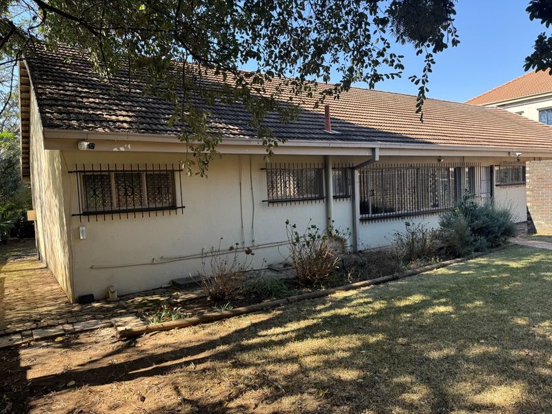 Rear view of the house featuring a tiled roof, security bars on windows, and a garden area with established landscaping.