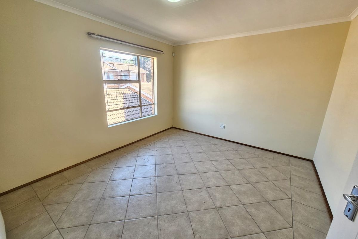 A bright, empty bedroom featuring neutral walls, tiled flooring, and a window providing natural light.