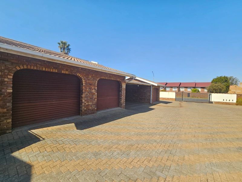 Exterior view of a townhouse complex featuring multiple roller shutter garage doors, a paved driveway, and secure perimeter fencing.