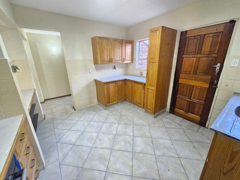 A functional kitchen featuring wooden cabinetry, tiled flooring, and a tiled splashback, offering a blank canvas for potential modern updates.