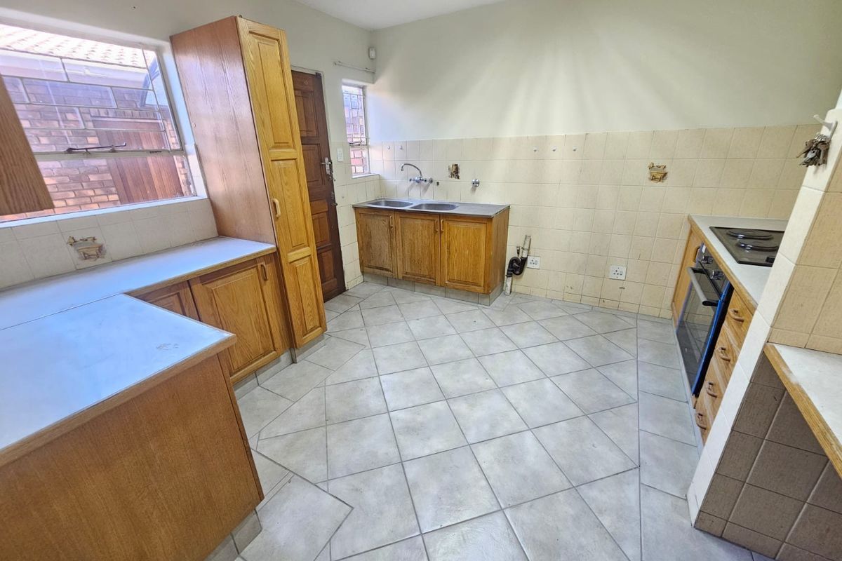 A dated kitchen featuring wooden cabinetry, tiled flooring, and built-in cooking appliances, offering a functional layout ready for modernization and cosmetic updates.
