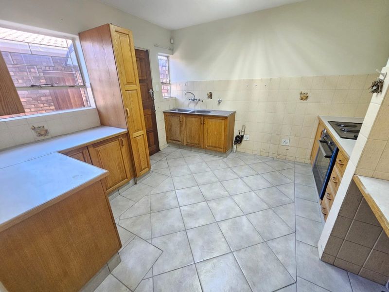 A dated kitchen featuring wooden cabinetry, tiled flooring, and built-in cooking appliances, offering a functional layout ready for modernization and cosmetic updates.