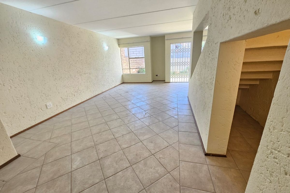 An empty, open-plan living area featuring tiled flooring, textured walls, and an integrated staircase, offering a blank canvas for renovation.