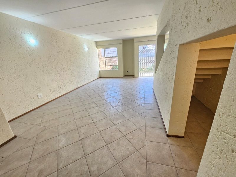 An empty, open-plan living area featuring tiled flooring, textured walls, and an integrated staircase, offering a blank canvas for renovation.
