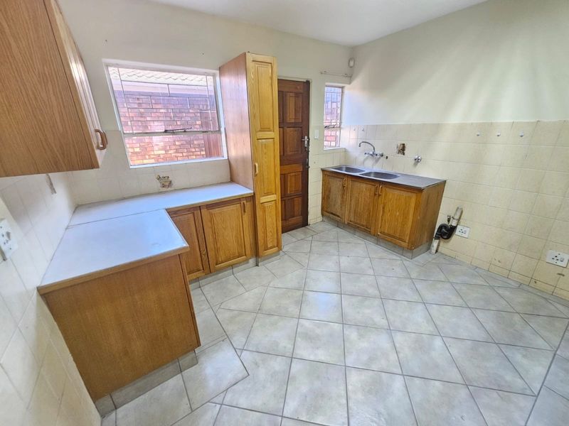 A functional kitchen space featuring wooden cabinetry, a double basin sink, and tiled flooring, offering a blank canvas for potential renovation and modernization.