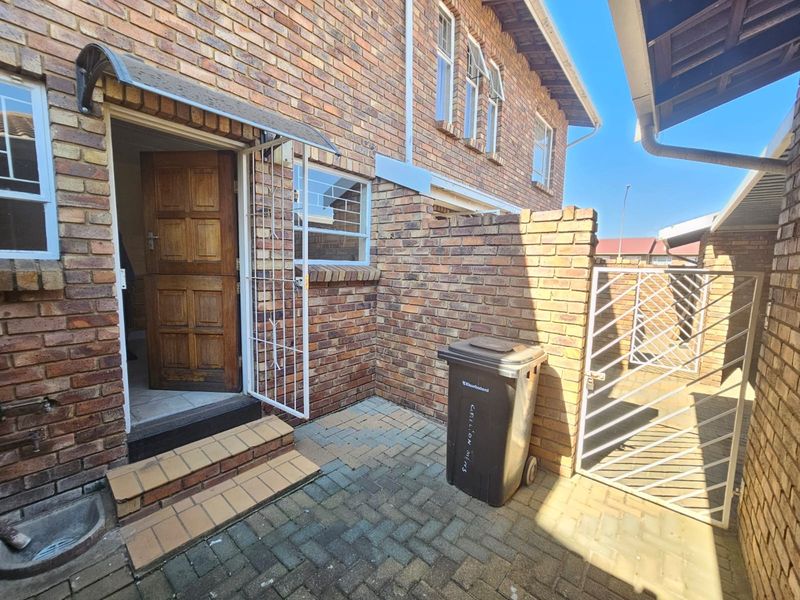 A rear courtyard area featuring face brick walls, paved flooring, a security gate, and a timber entrance door with a protective awning.