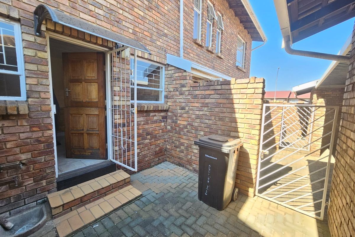 A rear courtyard area featuring face brick walls, paved flooring, a security gate, and a timber entrance door with a protective awning.