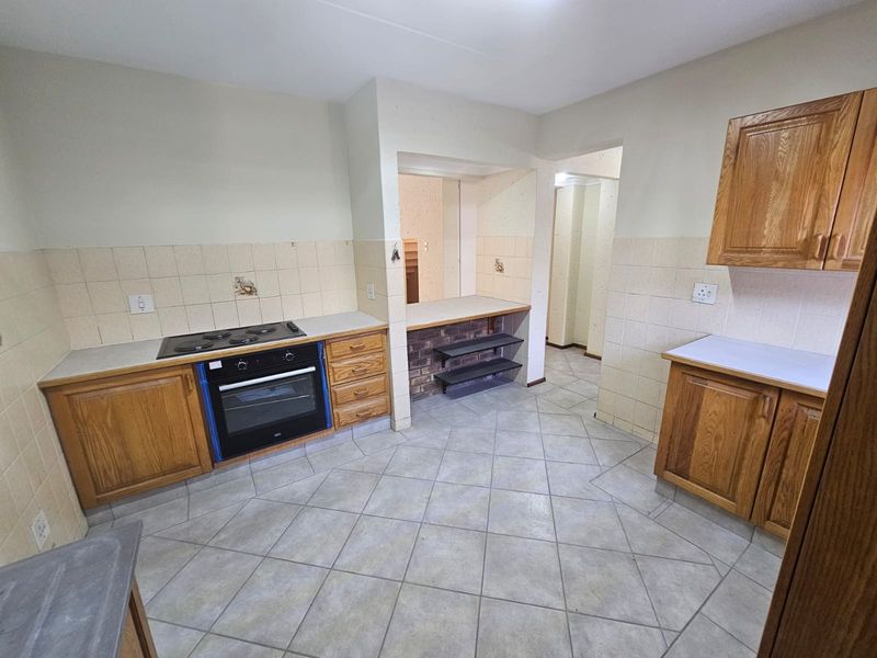 A functional kitchen featuring built-in wooden cabinetry, a ceramic tile backsplash, an integrated oven and hob, and durable ceramic floor tiles.