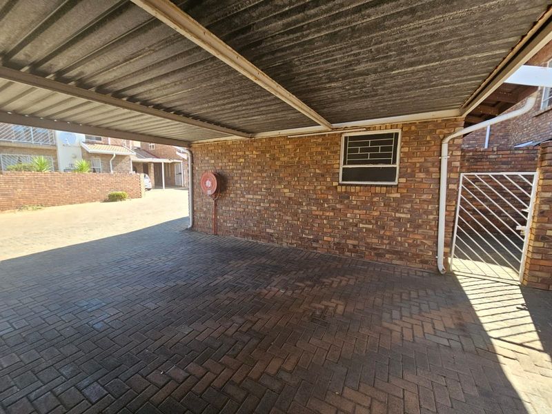 A covered carport area featuring facebrick walls, durable brick paving, and a functional fire hose reel, providing secure off-street parking.