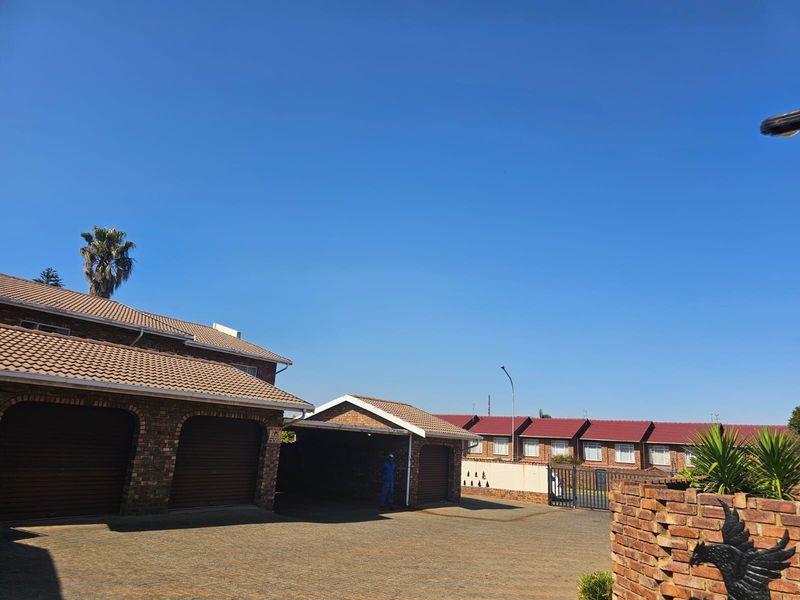 Front exterior view of the townhouse complex featuring brick facades, tiled roofing, paved driveway, multiple garage doors, and a covered carport area.
