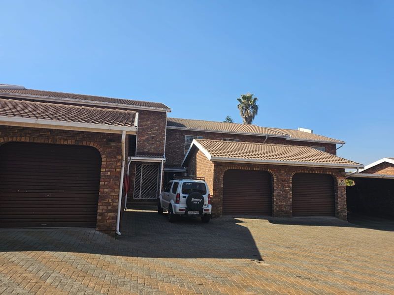 Front exterior view of a townhouse featuring a face brick facade, tiled roof, and a triple garage with a paved driveway.