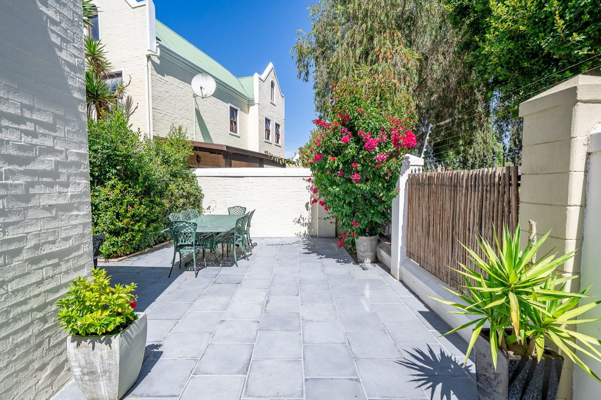 A private rear courtyard featuring grey stone paving, established garden beds, and secure boundary walling with timber screening.