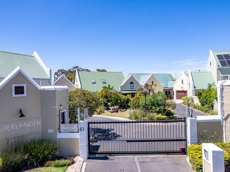 Front entrance view of Vierlanden Estate featuring a secure gated access point, electric fencing, and well-maintained residential buildings with pitched roofs.