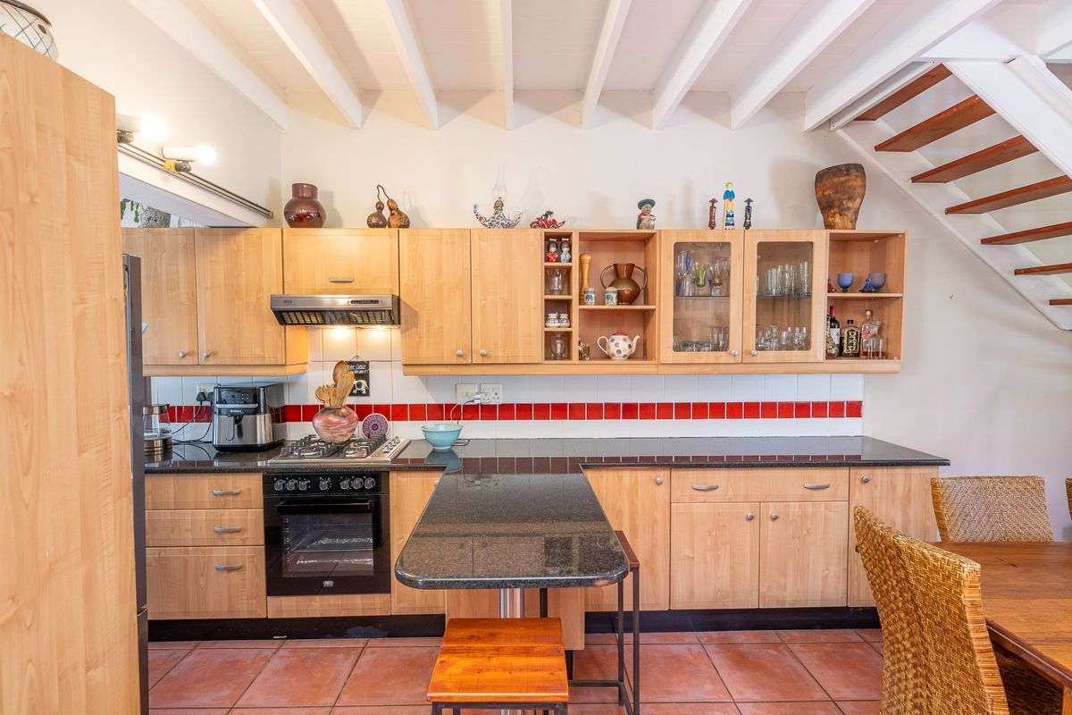 A functional kitchen featuring light wood cabinetry, granite countertops, a gas hob, and a tiled backsplash, set under an exposed beam ceiling.
