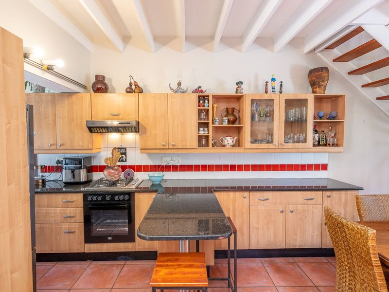 A functional kitchen featuring light wood cabinetry, granite countertops, a gas hob, and a tiled backsplash, set under an exposed beam ceiling.