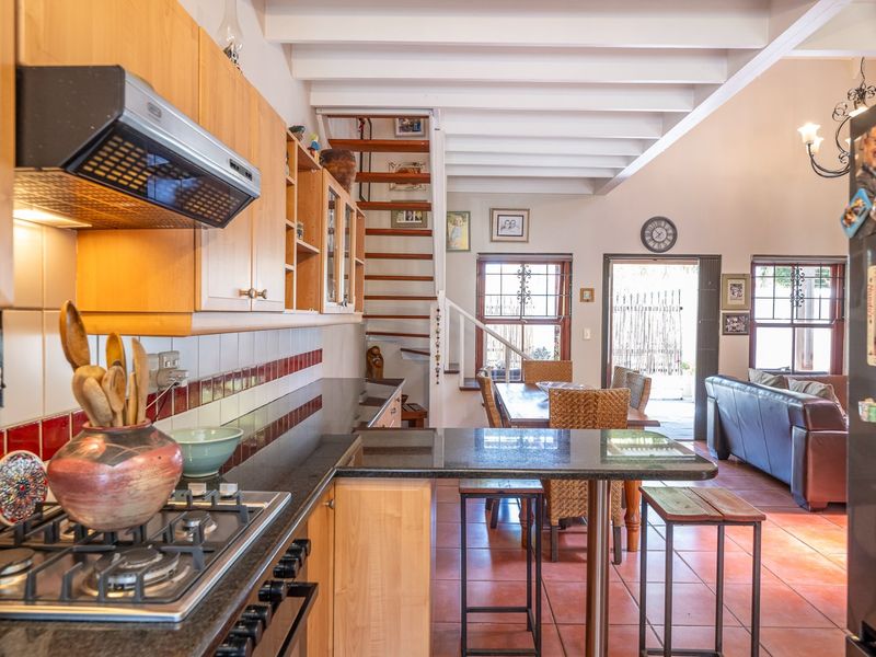 Open-plan kitchen and living area featuring light wood cabinetry, granite countertops, gas hob, exposed ceiling beams, and terracotta flooring with a spiral staircase.