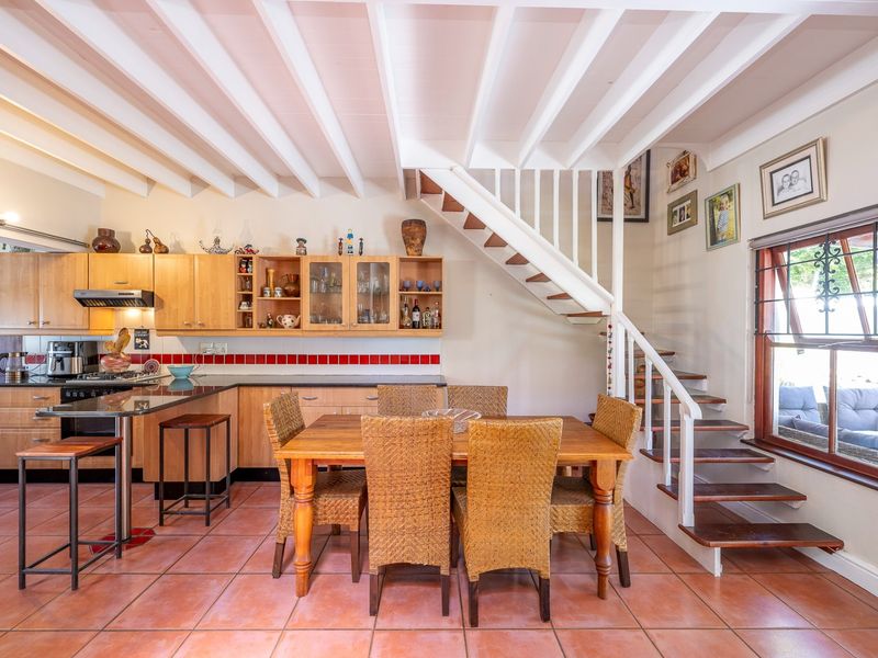 Open-plan kitchen and dining area featuring exposed ceiling beams, wooden cabinetry, granite countertops, and a staircase leading to the upper level.