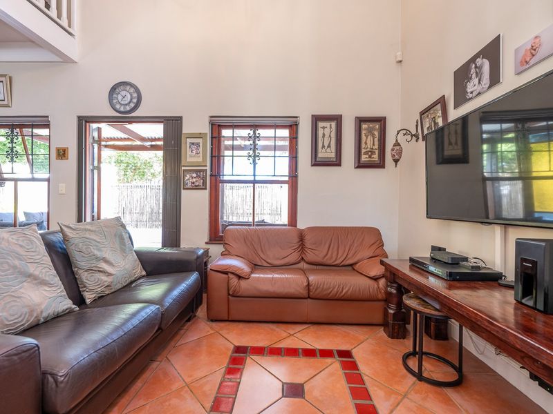 A living room featuring high ceilings, terracotta tile flooring, and access to an outdoor area through timber-framed doors with security bars.