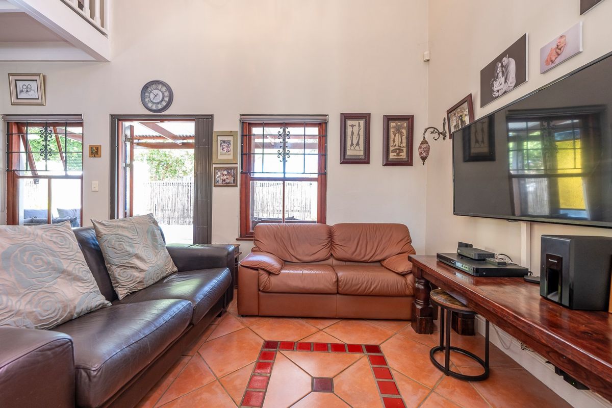 A living room featuring high ceilings, terracotta tile flooring, and access to an outdoor area through timber-framed doors with security bars.