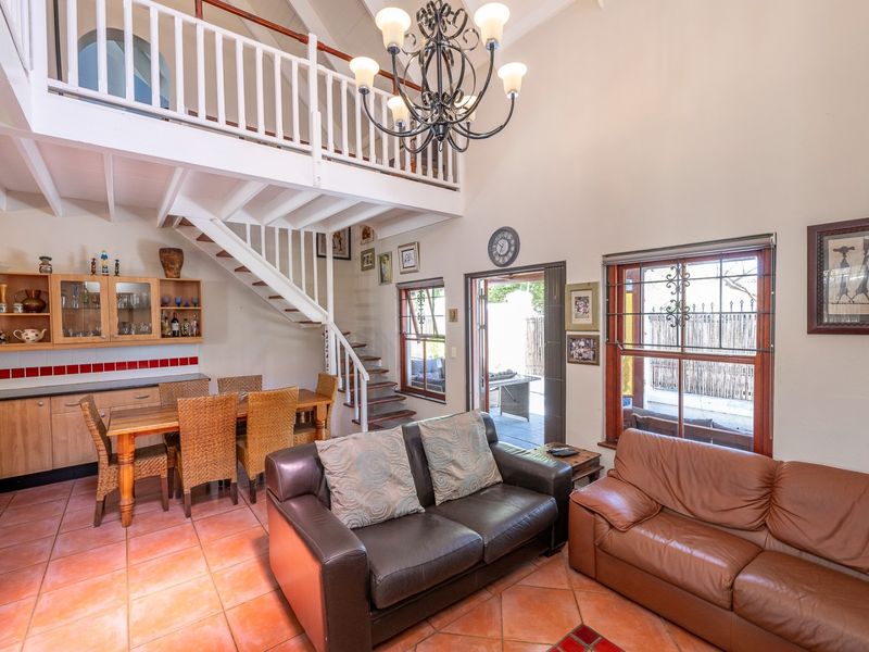 Open-plan living and dining area featuring a mezzanine level, timber staircase, tiled flooring, and built-in cabinetry with direct access to an outdoor patio.
