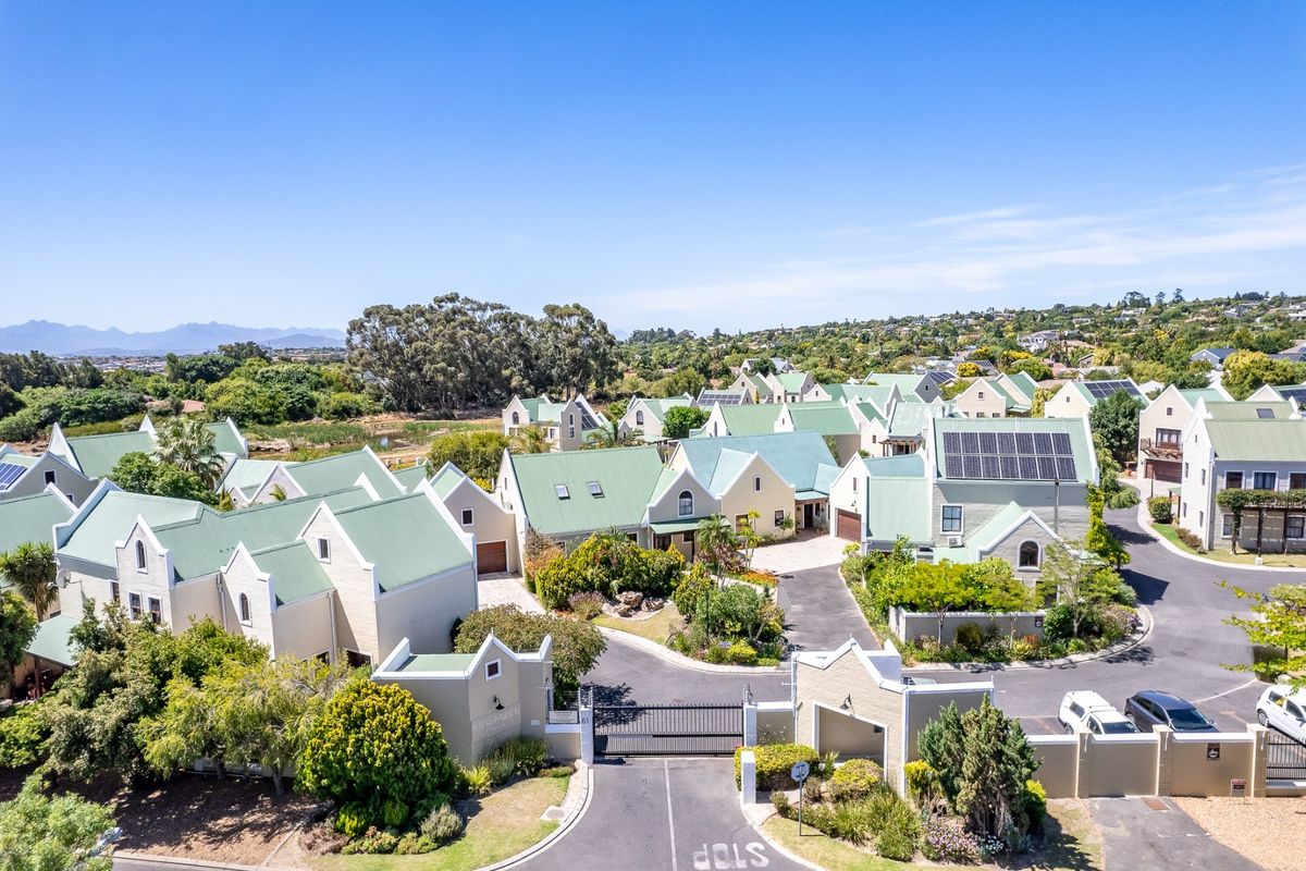 An aerial view of a residential estate featuring multiple homes with pitched roofs, solar panels, and a secure gated entrance.