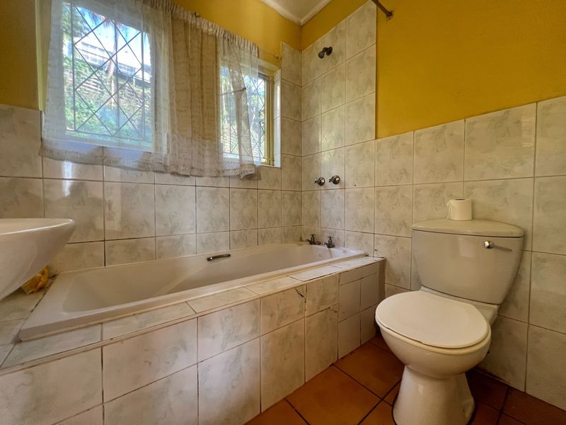 A functional bathroom featuring a built-in bathtub with shower, pedestal basin, and toilet, finished with tiled walls and flooring.