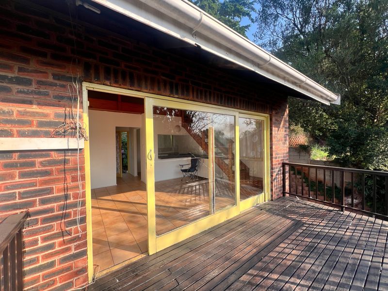 A wooden deck patio featuring sliding glass doors leading into the cottage interior, with exposed brickwork and a timber balustrade.