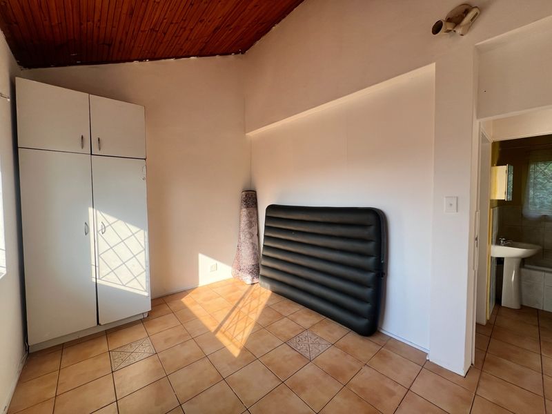 A bedroom featuring tiled flooring, a timber ceiling, and a built-in wardrobe, with direct access to an adjoining en-suite bathroom.