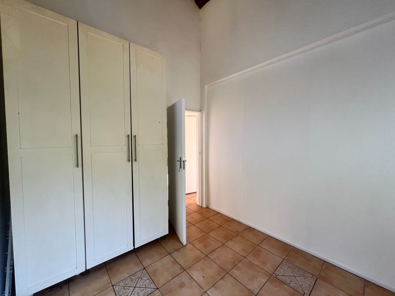 A vacant bedroom featuring high ceilings, tiled flooring, and built-in cupboards, offering a blank canvas for personalization.