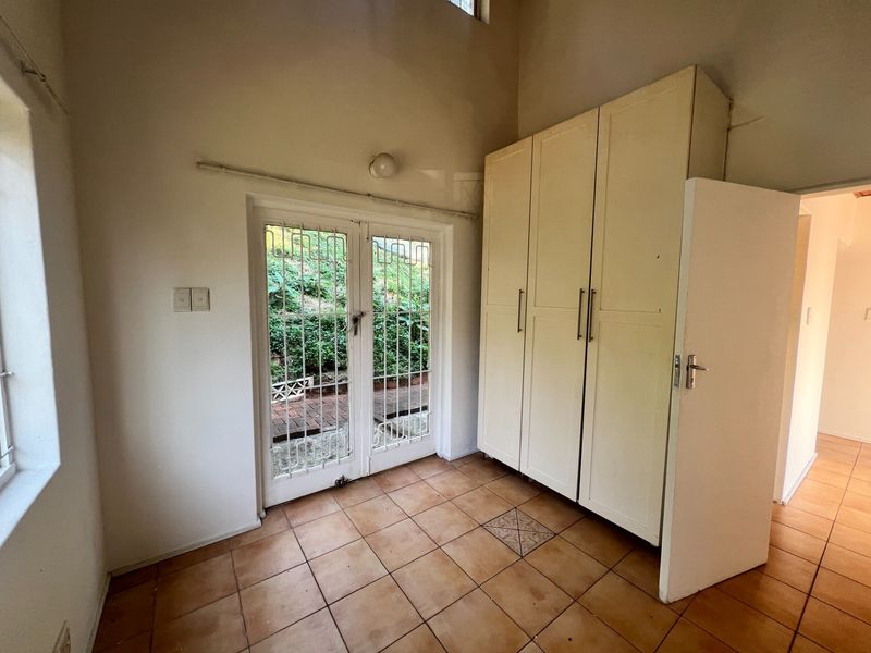 An entry area featuring tiled flooring, built-in storage cupboards, and a secure glass door providing access to the rear garden.
