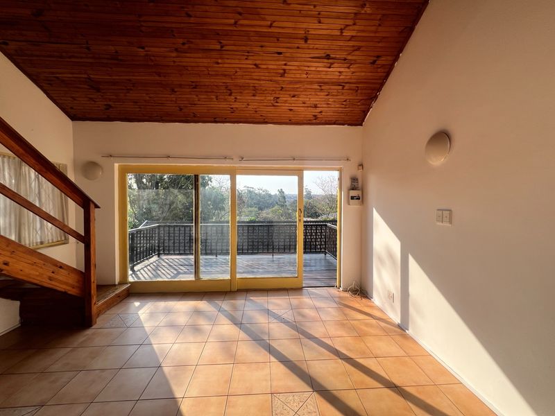 Spacious living area featuring a vaulted timber ceiling, tiled floors, and large sliding doors opening onto an outdoor deck with scenic views.
