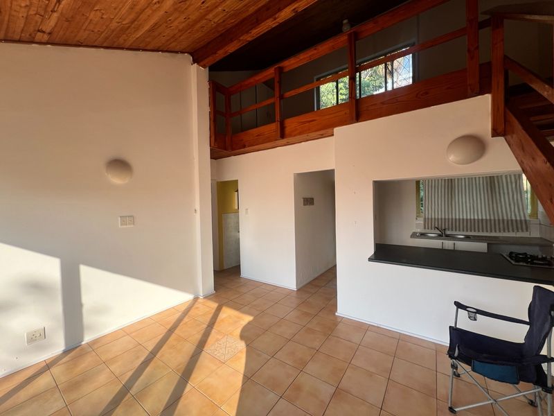 Open-plan living area featuring a timber-clad vaulted ceiling, mezzanine level with wooden balustrade, and a convenient kitchen pass-through with tiled flooring.