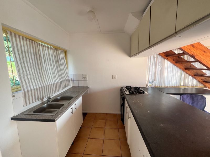 Functional kitchen featuring a double sink, gas hob, ample cabinetry, and tiled flooring, with an adjacent wooden staircase leading to the upper level.